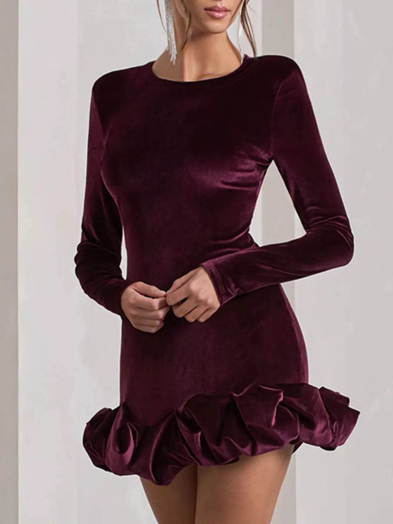 Burgundy velvet dress with long sleeves and ruffled hem on a plain background