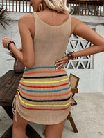 Woman wearing a beige knit dress with colorful striped bottom in an outdoor setting.