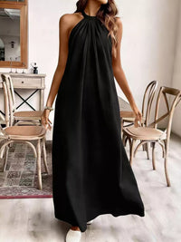 Woman wearing a black halter neck dress in a room with wooden chairs and a mirror.