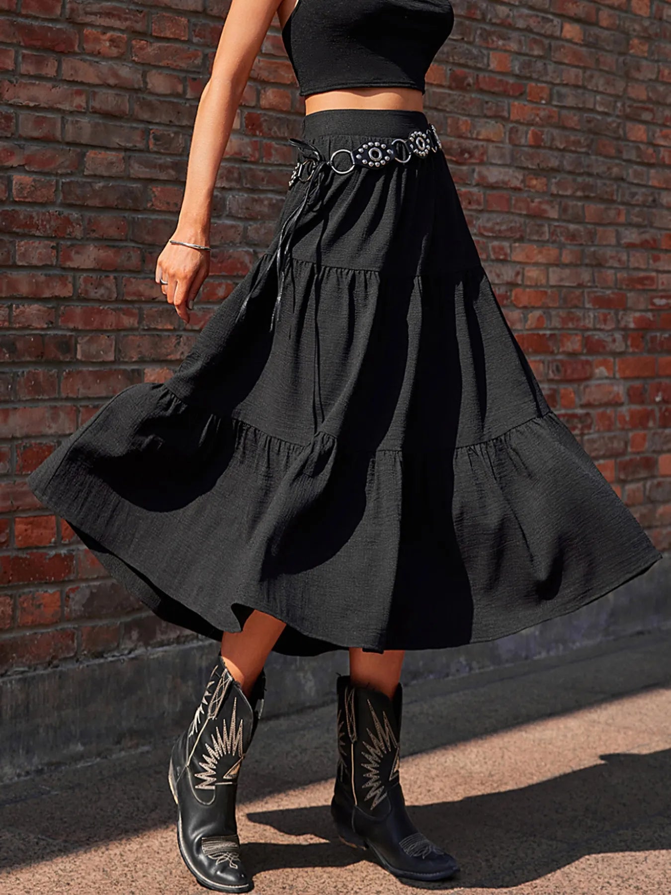 Person wearing a black skirt and boots against a brick wall.
