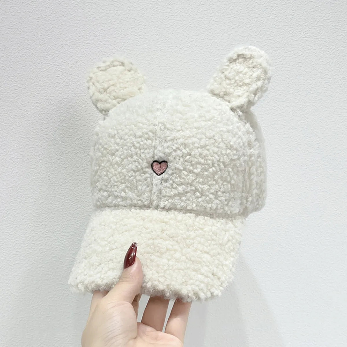 White fluffy hat with bear ears held by a hand against a light gray background