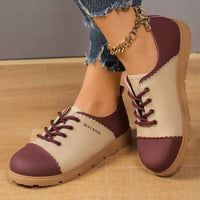 Pair of maroon and beige shoes worn with denim jeans on a wooden floor.