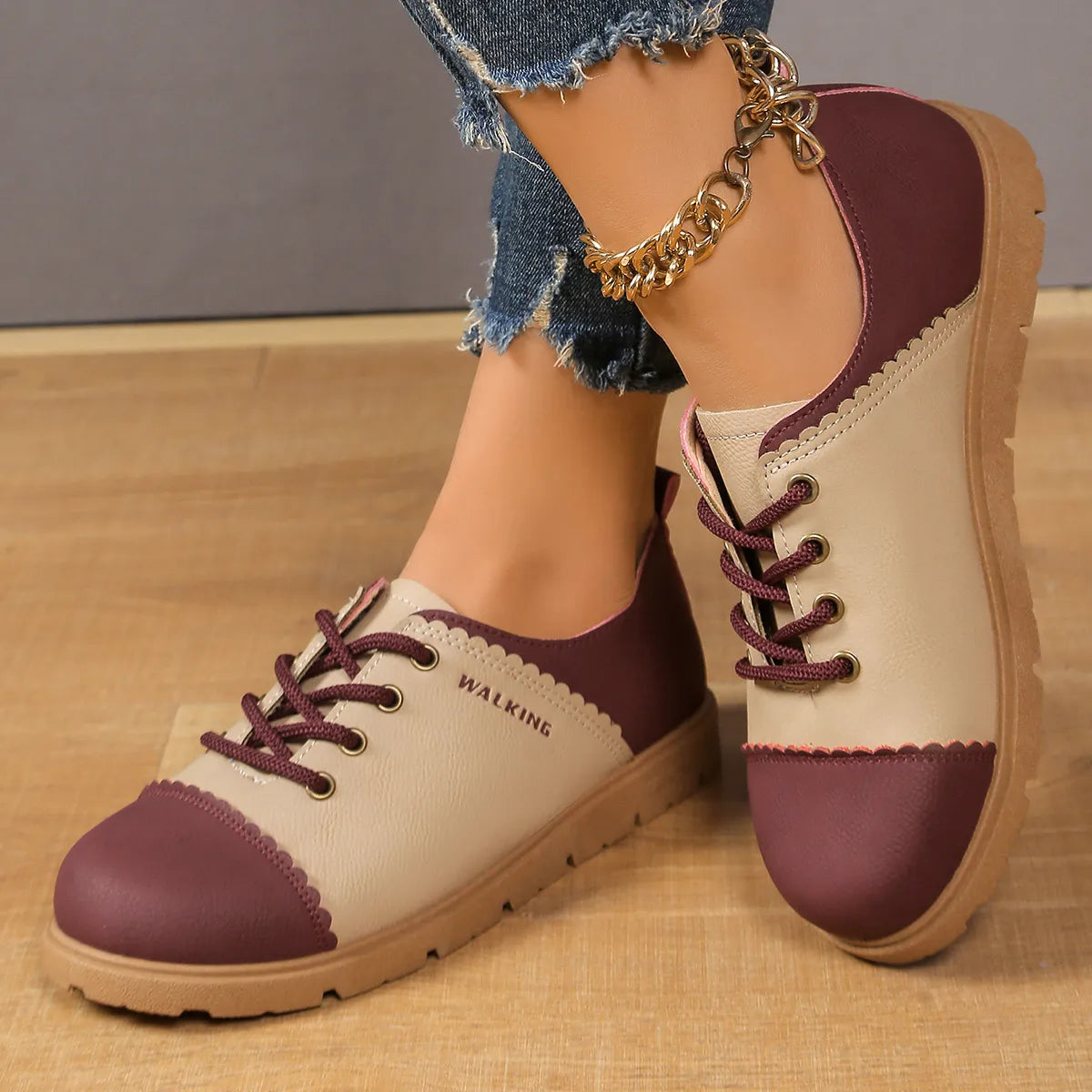Pair of maroon and beige shoes worn with denim jeans on a wooden floor.