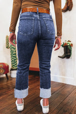 Person wearing blue jeans with a brown top and white shoes on a wooden floor.