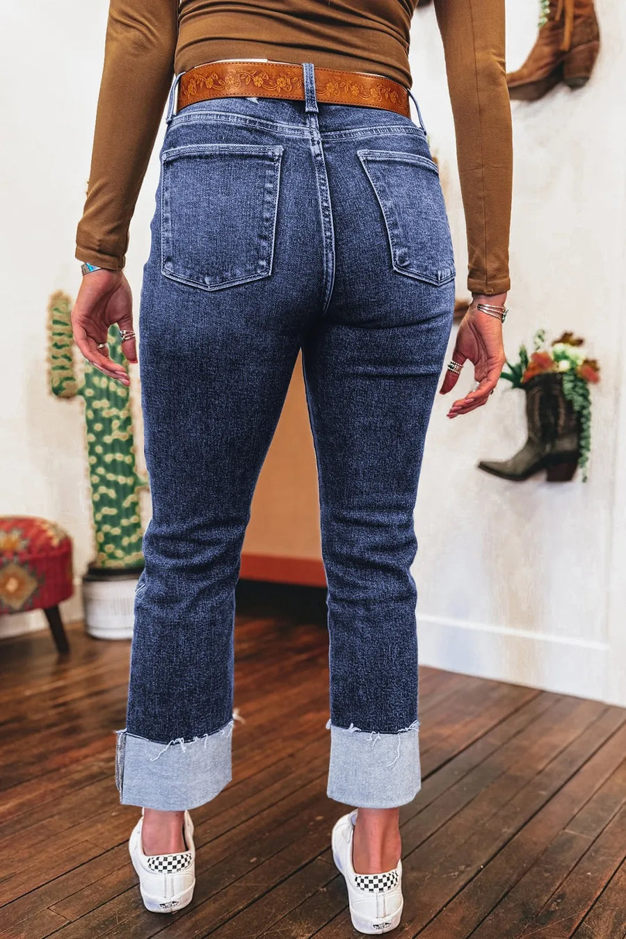 Person wearing blue jeans with a brown top and white shoes on a wooden floor.