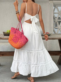 Woman in a white dress holding a colorful bag, standing outdoors.