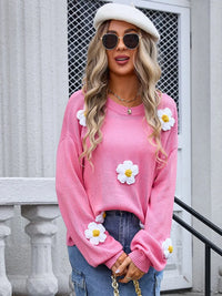 Woman wearing a pink sweater with white flower designs, standing outdoors.