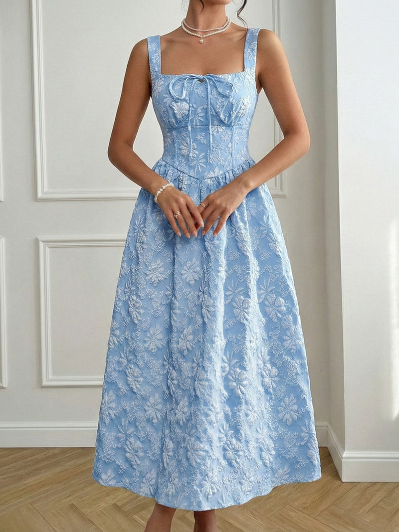 Woman wearing a blue floral dress against a white wall.