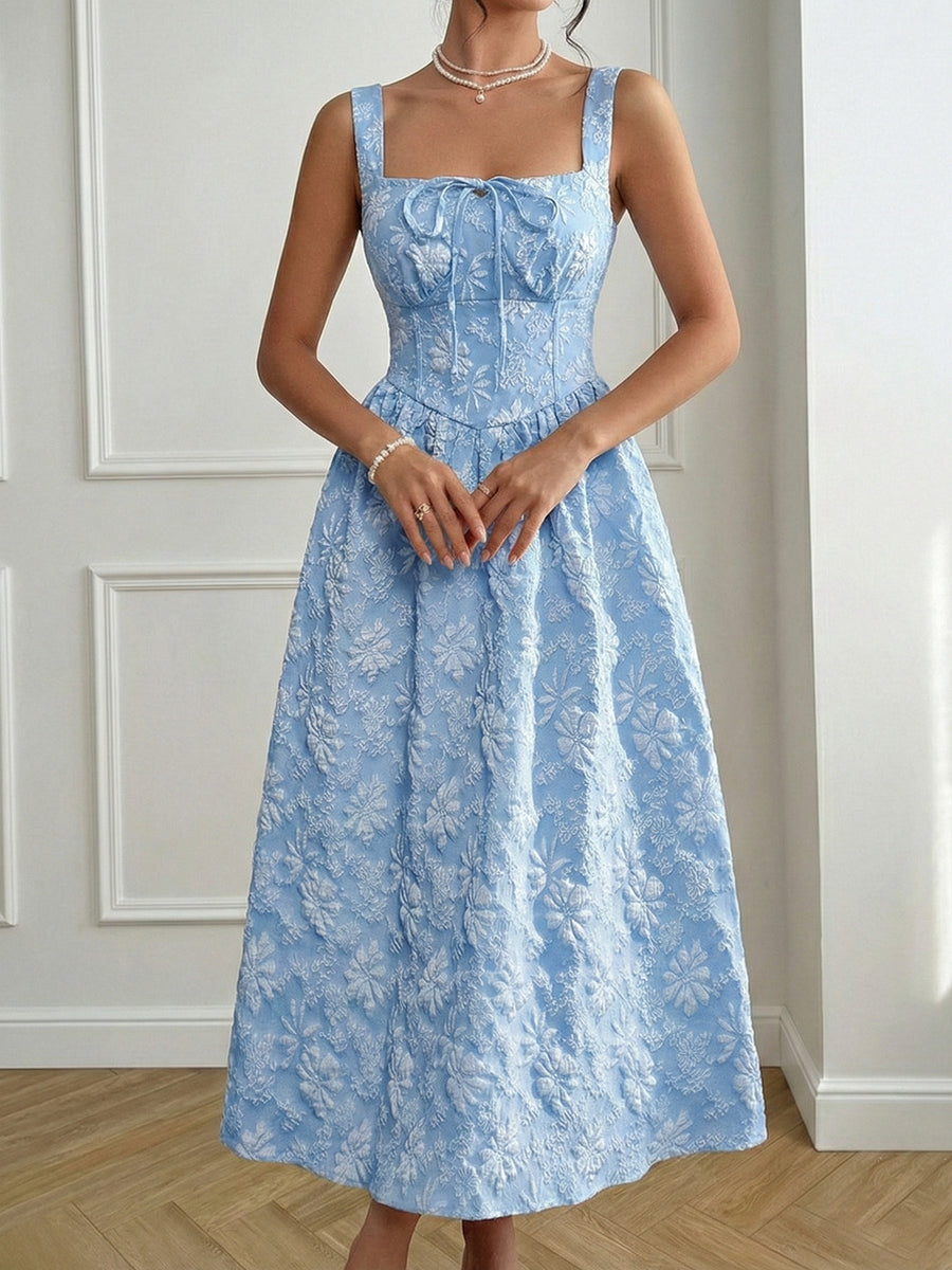 Woman wearing a blue floral dress against a white wall.