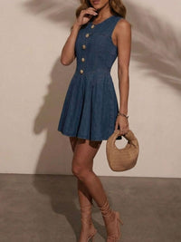 Woman wearing a blue dress with gold buttons, holding a beige handbag against a neutral background