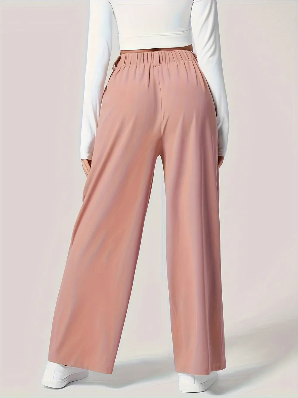 Person wearing pink wide-leg pants with a white top on a light pink background