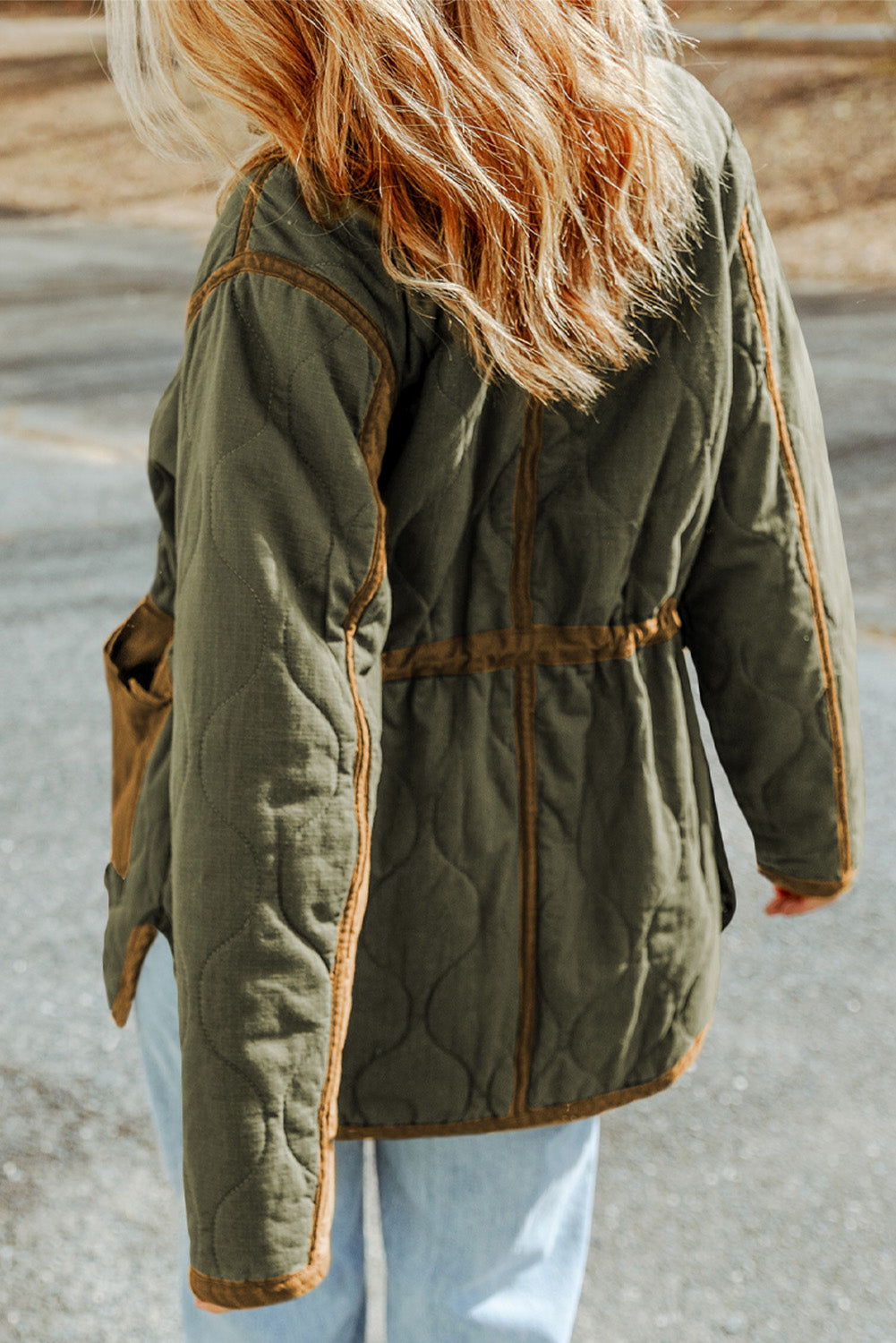 Person wearing a green quilted jacket with brown trim on a blurred background
