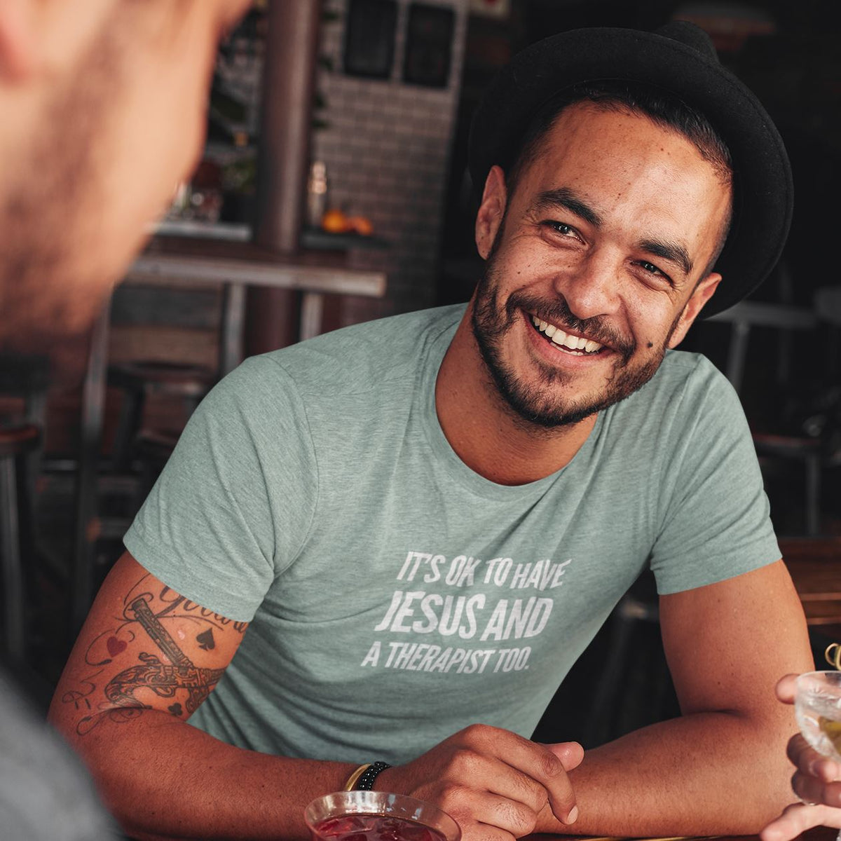 Man wearing a green t-shirt with text, sitting at a table in a casual setting.