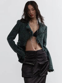 A person wearing a green frayed tweed jacket with a V-neck collar and pockets, paired with a black outfit. The jacket has a open front and the person is also wearing a necklace.