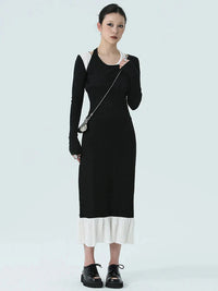 A person wearing a black long-sleeve dress with a cutout skirt, paired with white shoes and a across-the-body bag.