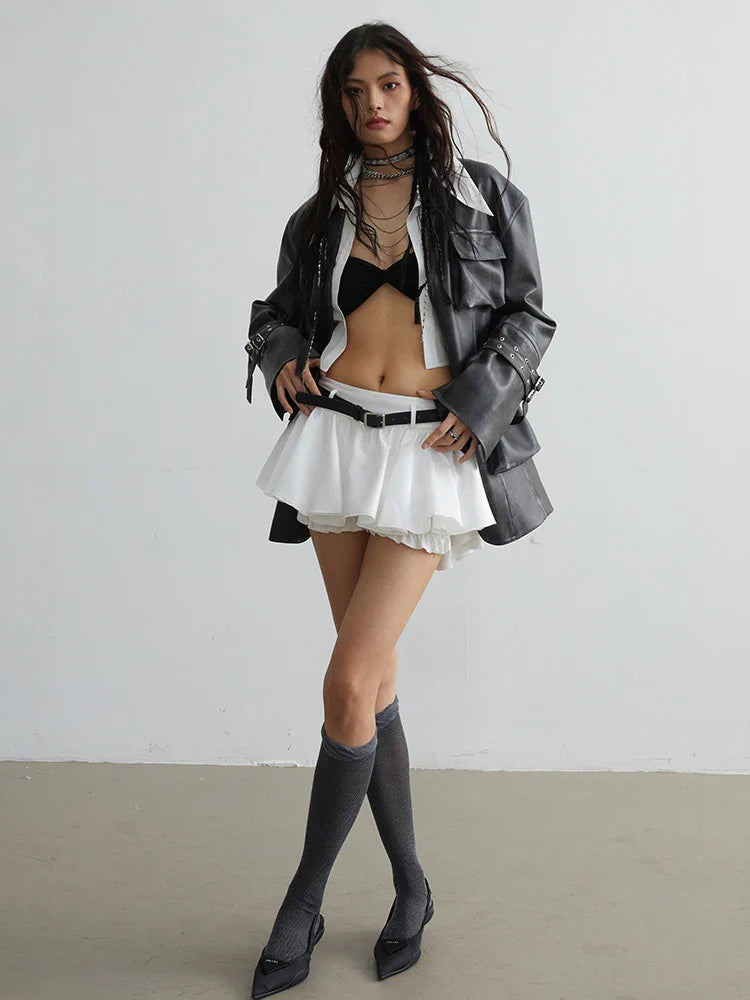 A model wearing a white ruffle mini skirt with a black belt and a leather jacket, paired with a black top and knee-high socks.