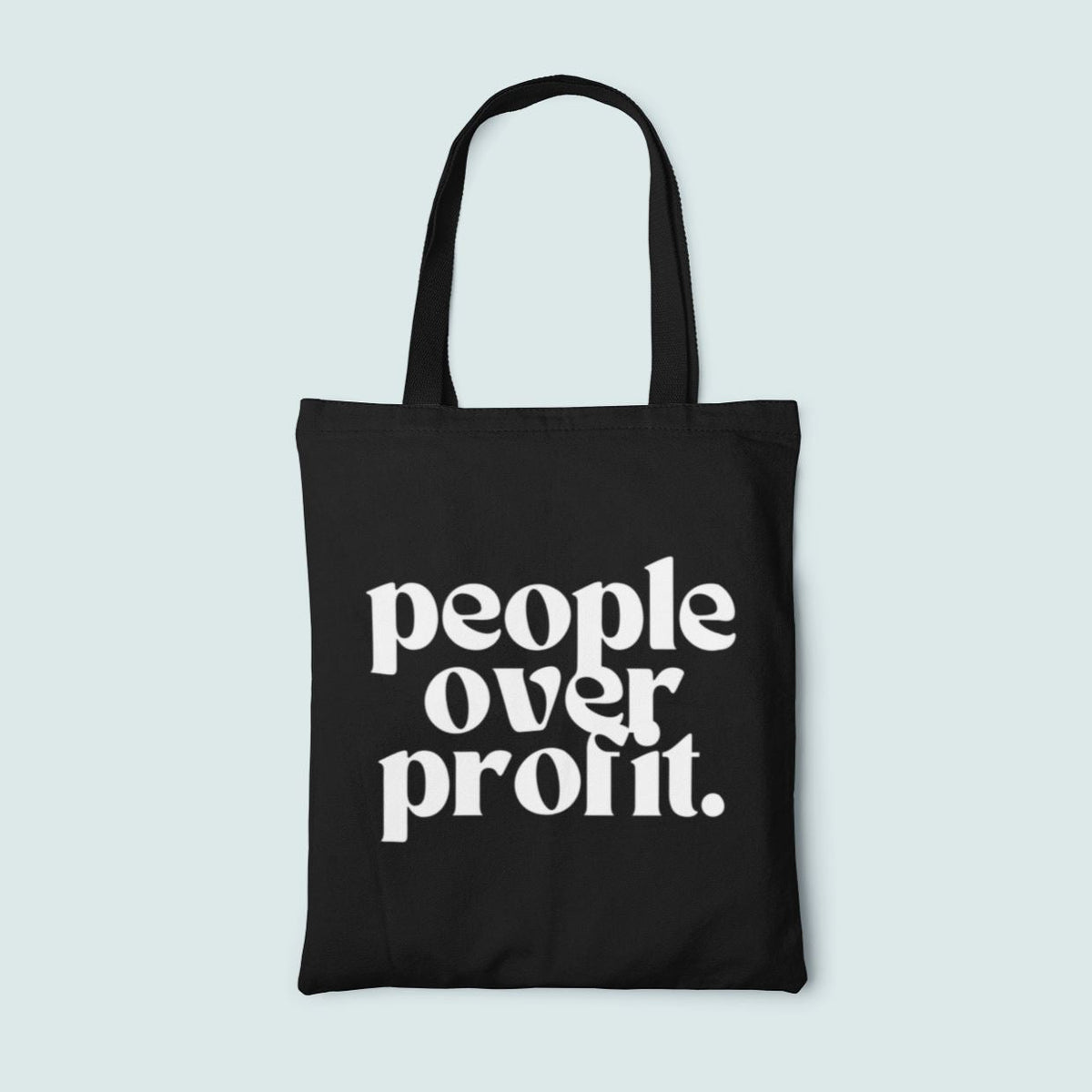 Black tote bag with 'people over profit' text on a light blue background