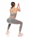 Woman in gray athletic wear performing a squat on a white background