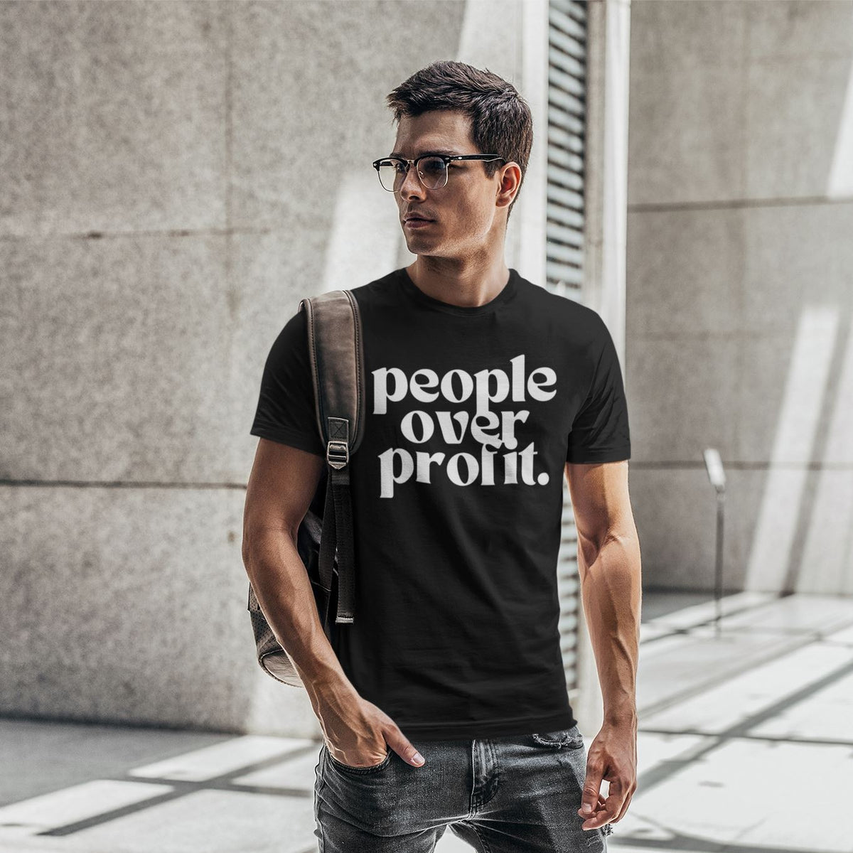 Man wearing a black t-shirt with 'people over profit' text, standing outdoors.