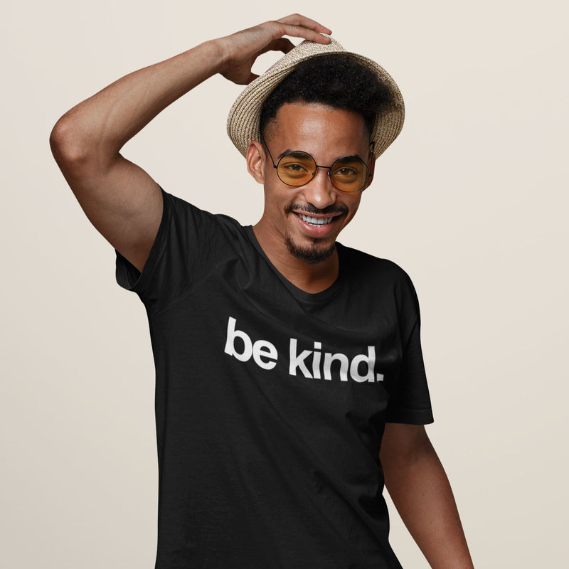 Man wearing a black t-shirt with 'be kind.' text, holding a straw hat against a beige background