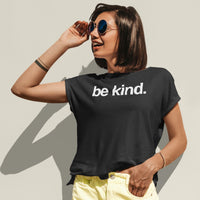 Person wearing a black t-shirt with 'be kind' text, holding sunglasses, against a plain background