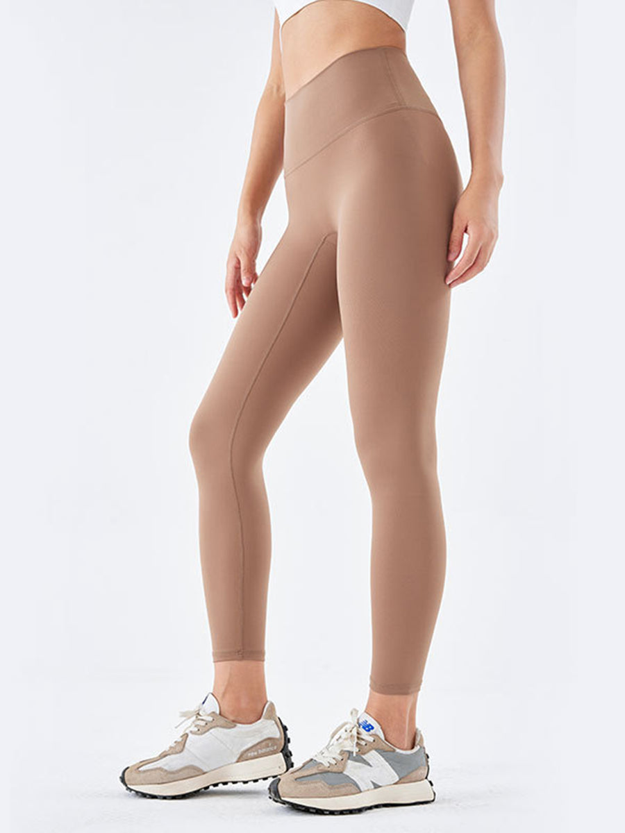A pair of beige wide waistband sports leggings, displayed on a model without showing the upper part of the body.