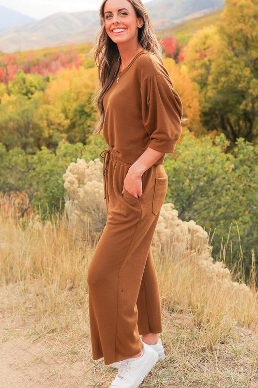 Model standing on the side of a country dirt road showing side view of Journey Pant- color is brown